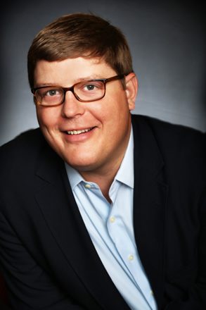 Smiling man in glasses and suit jacket.