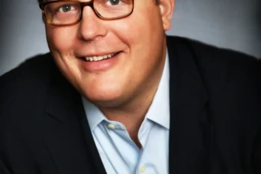 Man wearing glasses and a suit smiling.